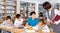 Group of school kids studying in school library with friendly female teacher