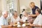 Group Of Senior Couples Enjoying Meal Together In Care Home With Home Help