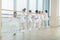 Group of seven little ballerinas standing in row and practicing ballet using stick on the wall