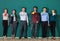 Group of six businesspeople colleague in modern company standing together in a row in front of the green wall and holding coffee