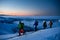 group of skiers with flashlights walking along mountain slope against the backdrop of picturesque evening sky