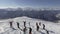 Group of skiers and snowboarders glides down off of snow capped ski hill top.