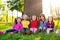 A group of small children in colorful clothes embracing sitting on the grass under a tree in a park laughing and smiling