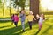 A group of small happy children run through the park in the background of grass and trees.