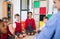 A group of small school kids with teacher sitting on the floor in class, holding hands.