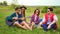 Group of stylish cheerful hipsters with guitar while sitting on a grass in the park.