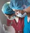 Group of surgeons at work operating in surgical theatre. Resuscitation medicine team wearing protective masks holding