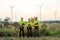 Group of technician workers stand with arm crossed and look at camera in front of windmill or wind turbine and evening light in