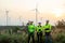 Group of technician workers stand with arm crossed and look to left side in front of windmill or wind turbine and evening light in