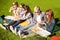 Group of teenage students eating pizza on grass