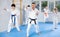 Group of teenagers in kimonos following karate sensei through kata exercises