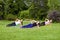 Group of three beautiful healthy slimy woman doing exersices on the green grass in the park, side palnk, looking at camera with