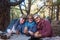 Group of three retired people smiling and sitting at a wooden table in the forest. Pines in the background. A sandwich in the