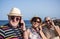 Group of three senior people in friendship enjoy sea excursion in summer vacation using smart phone- concept of active playful