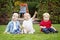 Group of three white Caucasian toddler children kids boys and girl sitting outside in summer autumn park by drawing easel