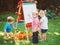 Group of three white Caucasian toddler children kids boys and girl standing outside in summer autumn park by drawing easel