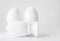 Group of three white ceramic eggs on stands or in egg-cups on white blurred background. Easter religious Christian symbol. Monochr