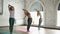 Group of three young women is practicing yoga doing elements of Sun Salutation Surya namaskara on yoga mats in light