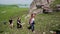 A group of tourists climb the steep slope of a rocky hill.