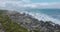 Group of tourists climbing on rugged coastal rocks. Orbit shot around people watching waves crashing on coast.