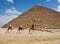 Group of tourists riding camels in front of an iconic Egyptian pyramid.