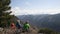 The group of tourists are sitting at the top of the hill and observing the montains with snow peaks.