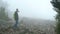 A group of tourists is walking along a gloomy foggy mountain covered with forest.