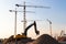 Group tower cranes, excavator silhouette at construction site, sunset sky background.Future residential high-rise complex