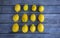 A group of twelve lemons arranged in a square pattern on a gray wood table