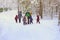 Group of unrecognizable litle kids with teachers of kindergarten, back to us, walk holding hands in snowy park, winter