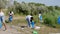 Group of volunteers picking up the garbage in the middle of the nature they holding big blue plastic bags wearing