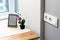 Group of white european electrical outlets and a switch located on a gray wall in a light modern kitchen with flower and e-book