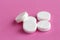 Group of white round medical pills on a pink background