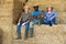 Group of workers resting on bales of hay after working on dairy farm