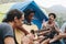 Group of young adult friends in camp site playing guitar