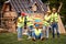 Group of young constructive workers cheering in front of wooden house. Hands in the air. Playful team. Teamwork. Wooden Skeleton