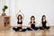 Group of young female friends sitting diagonally on floor on exercise mat, meditating together in traditional yoga pose