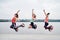 A group of young fit slim women in kangoo jumps, jumping in the air in front of city lake in summer. Three girls, wearing colorful