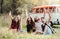 A group of young friends with drinks sitting on grass on a roadtrip through countryside.