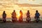 Group of young friends, motorcycle riders wearing helmets standing with their scooters on the coast, enjoying sunset