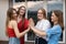 Group of young happy gorgeous women folding hands in stack, giving high five, clapping on window background. Friendship.