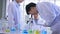 Group of young male and female Asian scientists wearing lab coat working together in lab using microscope to study and