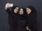 Group of young muslim women in fashionable dress with hijab using smartphone while taking selfie picture in front of