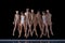 Group of young people, ballet dancers in beige bodysuits performing, dancing on stage against black background.