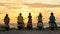 Group of young people, motorcycle riders wearing helmets standing with their scooters on the beach, watching sunset