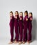 Group of young smiling girls gymnasts in dark red velvet sport costumes standing and posing over white background