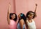 Group of young women wearing headphones and dancing together. Three females in casuals enjoying music against pink wall