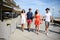 Groupe of young people man and woman walking on seaside of touristic resort during sunny summer day