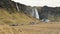 Groups of tourist visiting walk on pathways by beautiful waterfall of Seljalandsfoss in spring