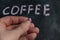 A grown man is holding a piece of pink chalk in his hand. Handwritten word COFFEE on black chalkboard